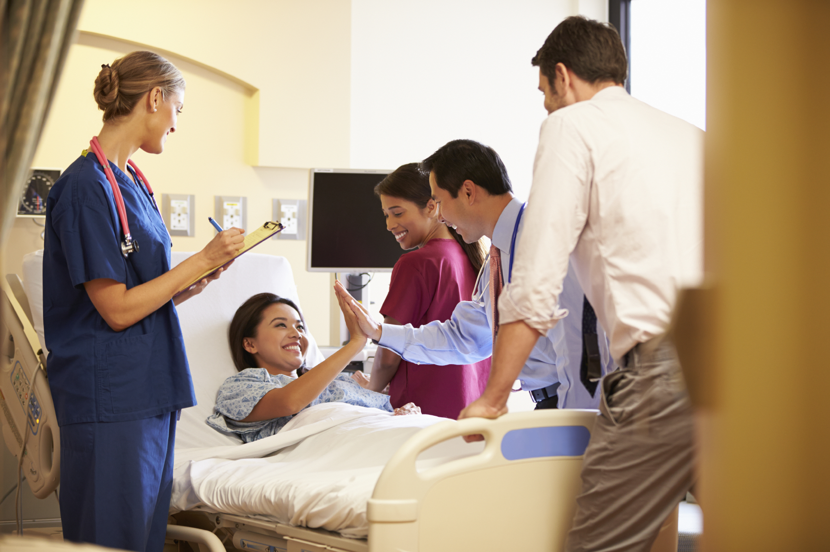 Medical Team Meeting Around Female Patient In Hospital Room